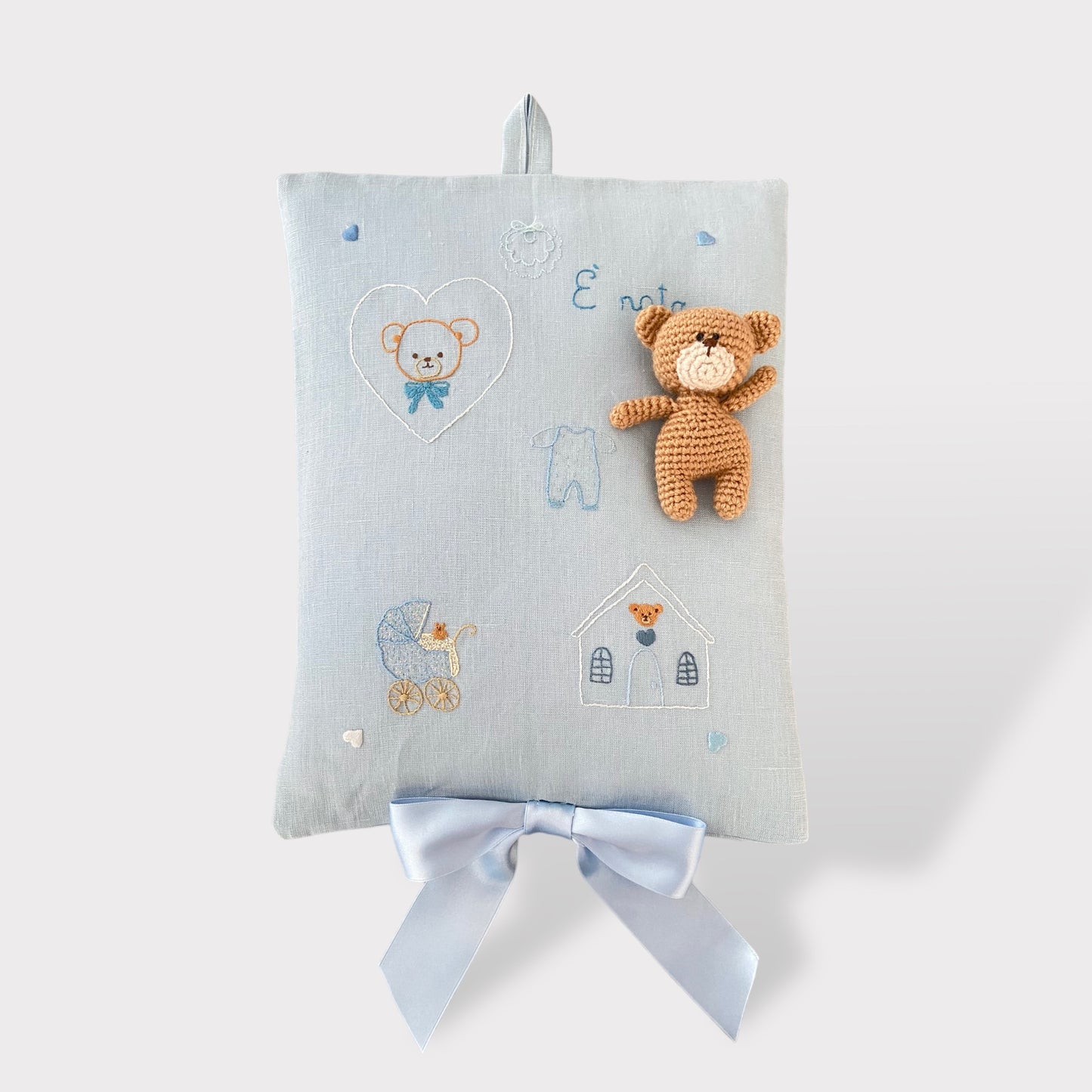 Fiocco nascita in puro lino sui toni dell'azzurro con il ricamo a mano di un dolce orsetto.