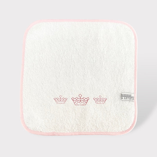 Asciuagamano in morbida spugna di cotone bianco con rifinitura rosa e ricamo di dolce corone da principessa.